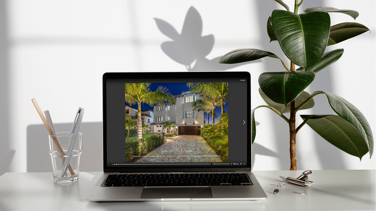 Laptop with luxury real estate magazine on screen sitting on desk with potted plants nearby